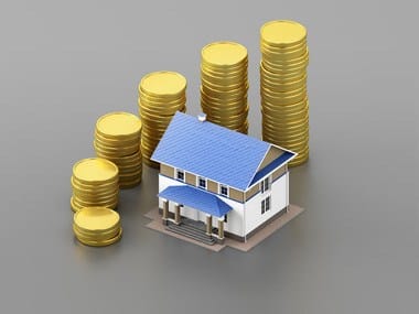 A miniature model house next to stacks of gold coins is a metaphor for home ownership