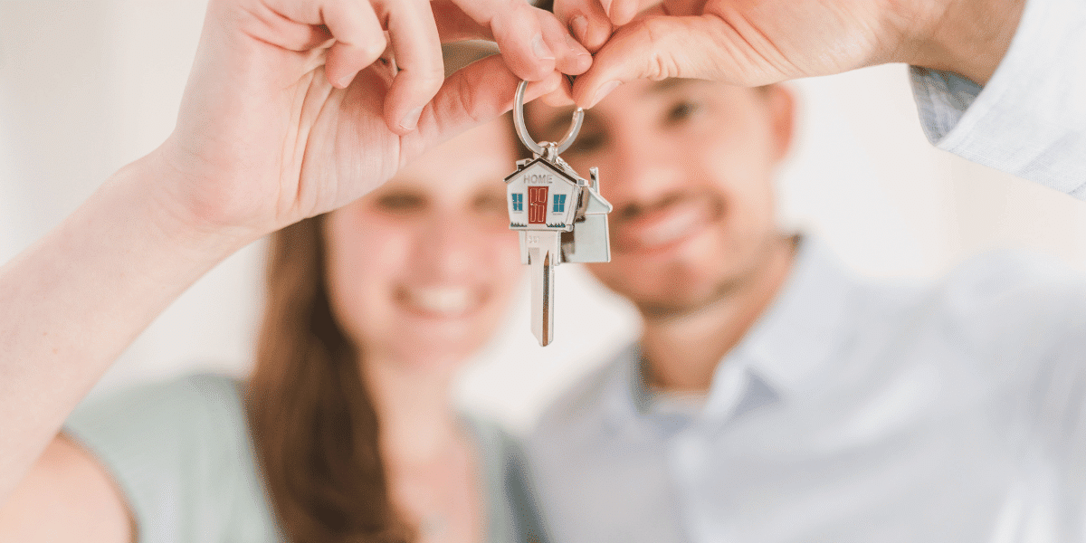 A young couple holding house keys in front of them
