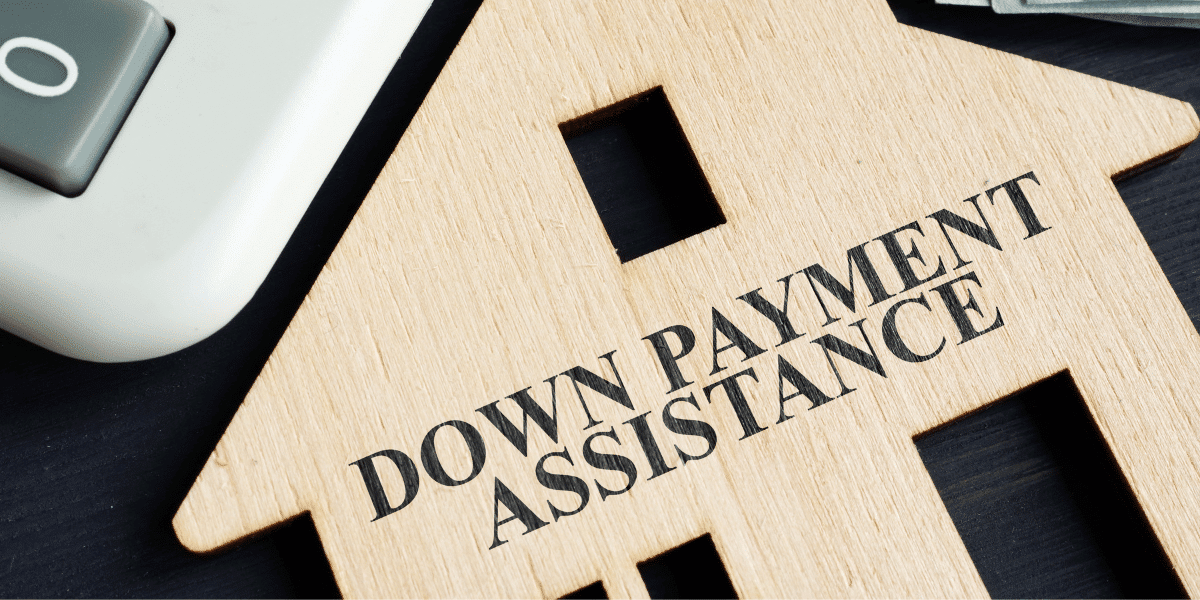 A desk with a wooden cutout of a house that says "down payment assistance" with a calculator next to it.