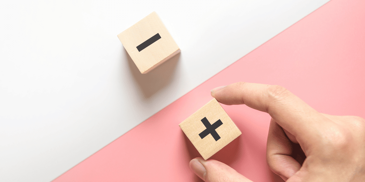 Two small wooden blocks, one with a plus and one a minus representing pros and cons
